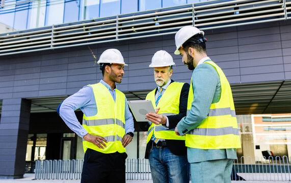 Construction site manager using digital tablet while having a discussion on building site with colleagues. Building project with senior engineer, male architect and business investor.