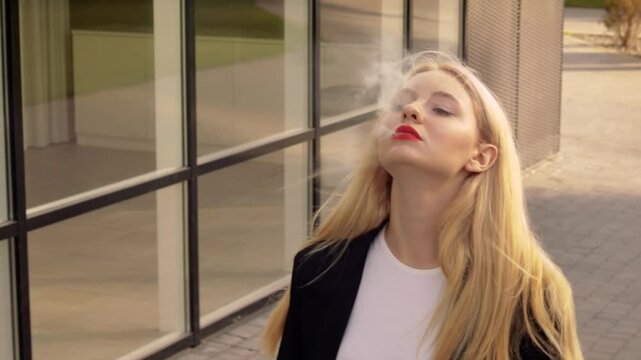 Young pretty woman standing outside street having break smoking trendy tobacco device electronic cigarette heater vape. Smoke and steam system with sticks inside. Harmful habit harm to health lungs