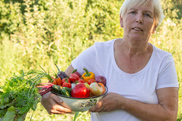 elderly woman in the garden with fresh vegetables in a bowl. Selective focus