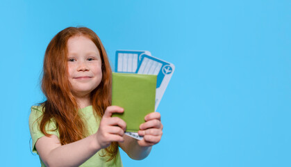Excited Girl With Red Hair Holds Travel Tickets and Green Passport on Blue Background