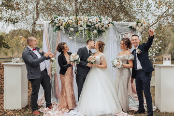 A group of people are posing for a picture in front of a wedding arch. The bride and groom are...