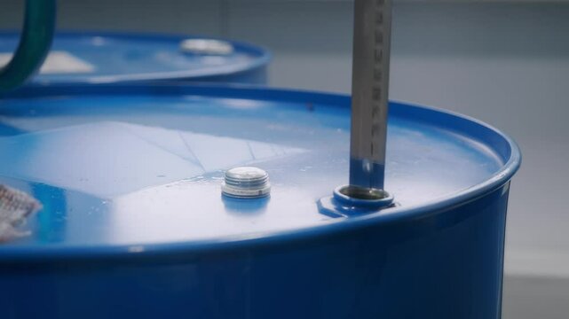 Video 4k. An industrial scene showing a measuring stick placed inside a blue drum with a white lid, emphasizing the careful measuring processes required in manufacturing environments.
