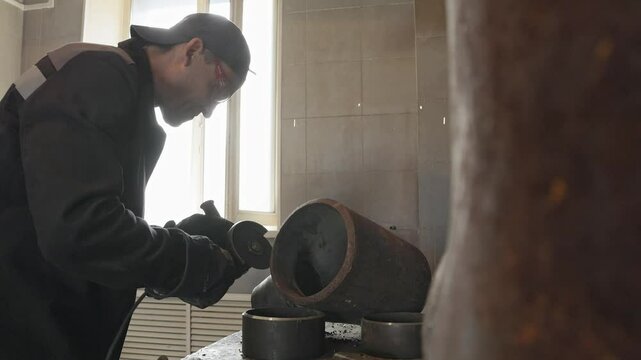 Video 4k. A man intensely grinds a thick metal pipe in an industrial workshop laden with various mechanical tools, showcasing craftsmanship, work ethic, and the skill required in metalworking.