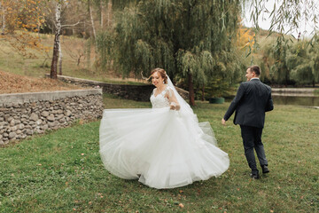 A bride and groom are walking in a grassy field. The bride is wearing a white dress and the groom is wearing a suit. Scene is happy and celebratory, as the couple is getting married