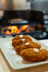 serving of typical Spanish croquettes, in the background you can see a grill with fire and food