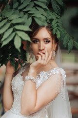 A woman is posing for a picture in a forest. She is wearing a white dress and has her hand on her...