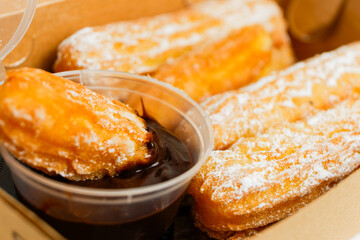 churros covered with sugar sprinkles with chocolate dipping on a box