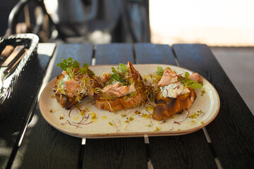 Fresh avocado toast with smoked salmon and poached eggs with grilled vegetables on plate on wooden table in city cafe. Healthy food and lifestyle. High quality 