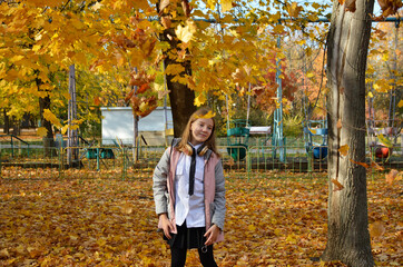 beautiful girl on a walk in the autumn park. the child is happy, having fun, smiling. From above, yellow maple leaves fly onto the girls head. active lifestyle and outdoor walks