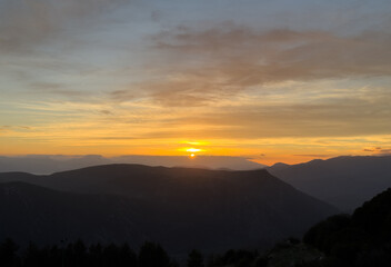 Fototapeta premium Sunrise, sunset over the silhouette of mountains. Dramatic colorful sky with clouds