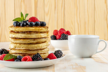 Delicious pancakes with fresh berries on white wooden table. Food concept.