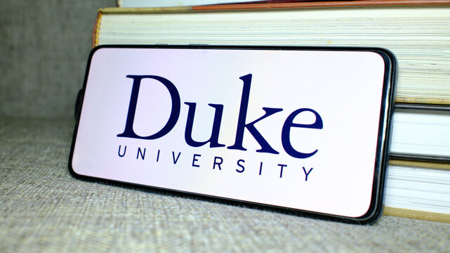 Duke University logo on phone screen with stack of books behind. London, UK, 08.25.2024