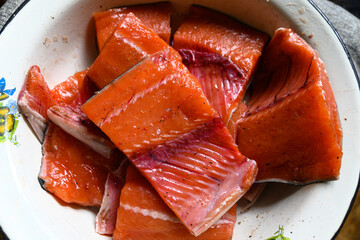 Pieces of raw salmon on the plate sprinkled with pepper and salt ready for cooking