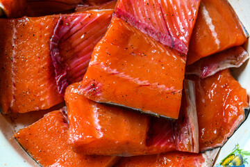 Pieces of raw salmon on the plate sprinkled with pepper and salt ready for cooking
