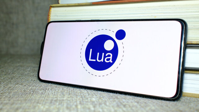 Lua logo on phone screen with stack of books behind. London, UK, 08.25.2024