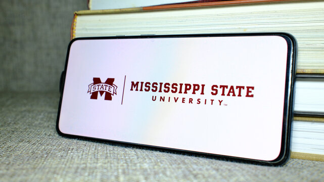 Mississippi State University (MSU) logo on phone screen with stack of books behind. London, UK, 08.25.2024