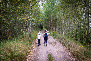 Obraz premium Friendly sisters walk hand in hand along a path in the forest in early autumn