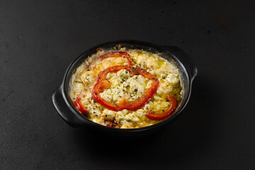 Grilled feta cheese with fresh tomato, bell pepper and oregano in plate on dark background.