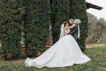 Fototapeta premium A bride and groom are standing in a lush green field, with the bride wearing a long white dress