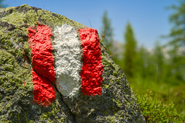 A red-white-red trail painted marker, indicating a hiking route in the Austrian Alps, set against a backdrop of mountain terrain.