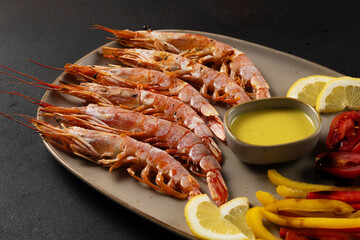 Grilled shrimps with lemon, paprika and sauce on dark background.