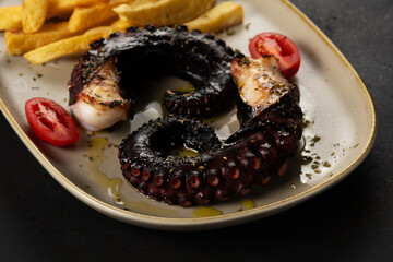 Grilled octopus tentacles with potatoes and herbs on a plate. On a black background.