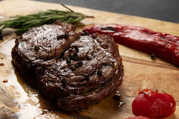 Tasty Rib Eye Black Angus served with pepper and herbs on wooden board.