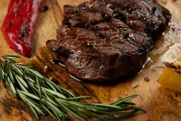 Grilled Rib Eye Black Angus served with pepper and herbs on wooden background.