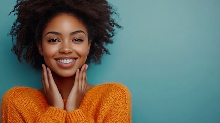 Fototapeta premium Touched beautiful smiling Afro American girl keeps palms on heart expresses appreciation pleasure and gratitude wears orange sweater models over blue background Confession in love conc : Generative AI