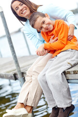 Happy, mother and kid on dock for portrait, love and tickling on harbour on vacation. Family, mom...