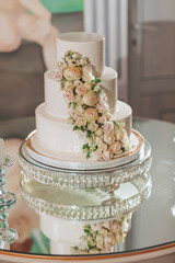 A three tier wedding cake with a floral design on top. The cake is placed on a silver tray and is surrounded by other items such as a vase and a candle. Scene is elegant and celebratory