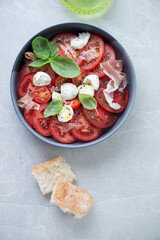 Italian caprese salad with torn prosciutto, top view on a grey granite background, vertical shot