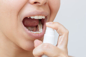 Close up of a young caucasian woman using spray to freshen a breath on a light background. Vitamins...