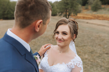 A bride and groom are standing in a field, the bride wearing a white dress and the groom wearing a blue suit