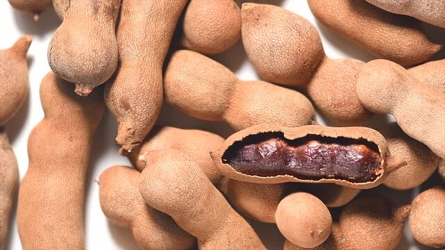 Tamarind tropical fruits background. Heap Fresh ripe dryed Tamarind pods (Tamarindus indica, Indian date), healthy vegan food. Top view, flat lay, rotating, slow motion. 