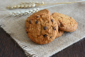 a cookie with chocolate chips on burlap texture with wheat on the background