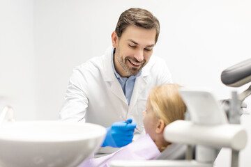 Little kid girl taking care of her teeth sitting in chair while male dentist examining whitening dental cavity, clinic office