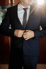 A man in a suit is getting ready to go out. He is wearing a blue suit and a white shirt. He is adjusting his tie and looking at the camera