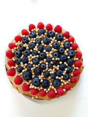 Delicious homemade round cake with caramel, decorated with blueberries, raspberries and golden beads, standing on white surface