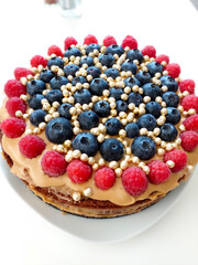 Mouthwatering chocolate cake decorated with blueberries, raspberries, caramel and golden beads standing on white background