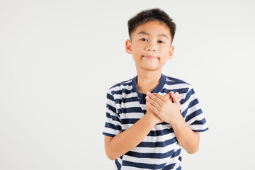 Happy young kid boy in casual clothes holding hands at chest close to heart meditation and smiling...
