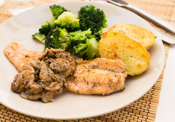 Fried river trout fillet with a complex side dish of broccoli, baked potatoes and mushroom sauce