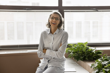 Laughing middle-aged professional businesswoman with short grey hair and eyeglasses posing for...