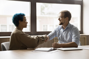 Two young smiling multiethnic business partners conclude agreement, making deal, establish...