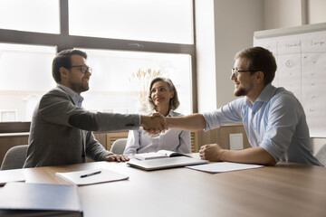 Two businessmen shaking hands finish meeting in office, congratulate each other on their...