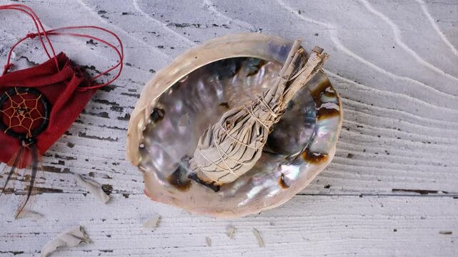 Burning white sage smudge stick (Salvia apiana) in an abalone shell. Lockdown shot.
