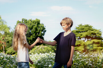 Obraz premium Happy family, brother gives flowers to his little sister at beautiful flower garden. Joyful kids, boy and girl have fun outdoor at public park. Sibling children enjoy spending time outside together.