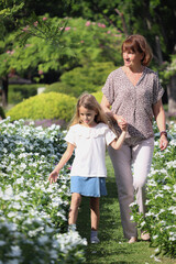 Fototapeta premium Happy family, grandchild and elderly grandma hold hands, walk through beautiful flower garden together. Joyful kid girl spend time outdoor with senior grandmother at public park. Child and elderly.