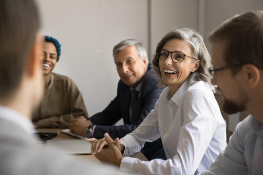 Happy middle-aged businesslady take part in meeting, review profit, discuss revenue growth, planning new products development and innovation strategy, laughing, joking, sharing light-hearted moments
