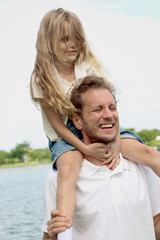 Obraz premium Father carrying cute daughter, joyful parent piggybacking his child girl at the park on summer holiday. Dad plays with kid and spends time outdoor together in beautiful garden. Happy family outside.